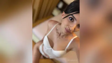 Young woman in white lace lingerie relaxing in a bright, cozy bedroom setting.