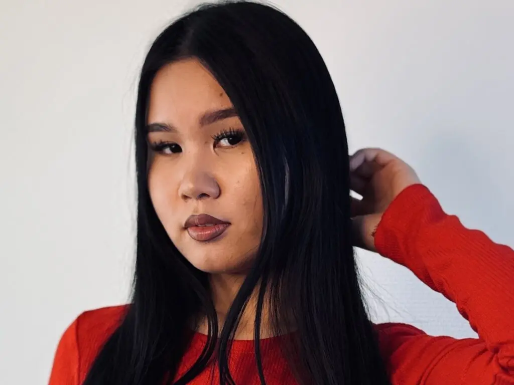 Young woman with long black hair wearing a red long-sleeve shirt against a plain white background.