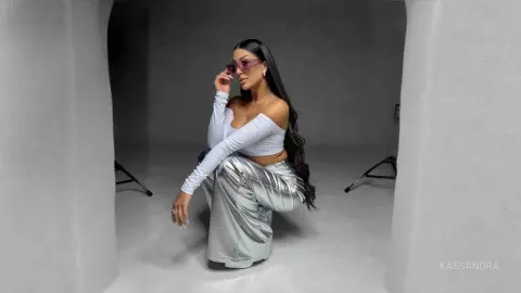 Stylish woman in silver metallic trousers and white crop top posing in a minimalist grey studio setting.