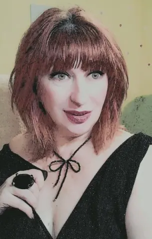 Woman with red bangs in a black glitter dress and black necklace posing with a soft expression.