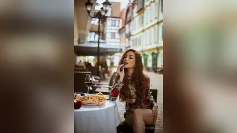Stylish woman in a floral dress enjoying red wine at an outdoor cafe in a European city setting.
