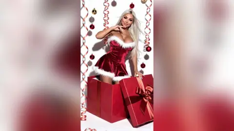 Blonde woman in a red velvet Santa outfit sitting in a large red gift box for a festive Christmas photoshoot.