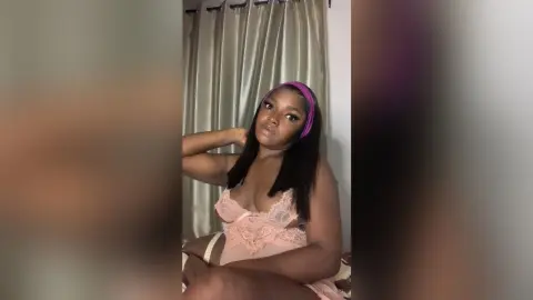 Young woman in pink lace lingerie and headband posing in a bedroom setting with a soft, intimate mood.