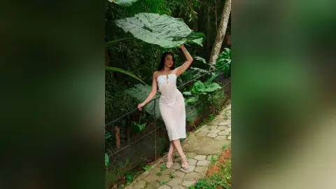 Elegant woman in a white lace midi dress standing in a lush tropical garden setting.
