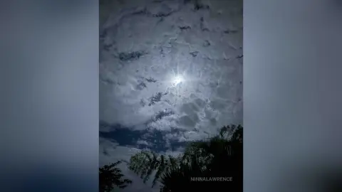 Dramatic moonlight shining through thick, dark clouds over a silhouette of palm trees at night.