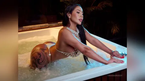 Glamorous woman in white pearl bikini relaxing in a bubbling outdoor hot tub at night.