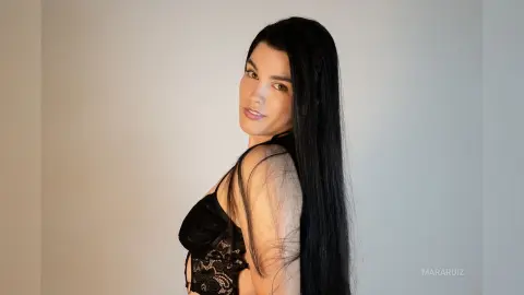 Elegant woman with long black hair wearing a black lace corset in a minimalist studio setting.