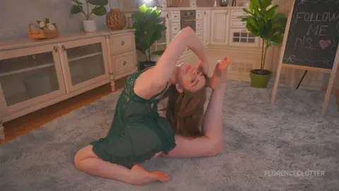 Young woman in a green lace chemise performing yoga stretches on a grey rug in a cozy, bright living room.