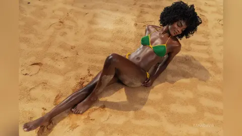 Beautiful Black woman in a green bikini relaxing on a sunny sandy beach.