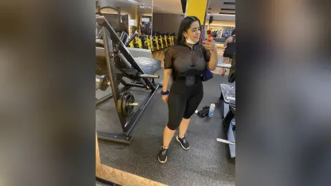 Curvy woman in black athletic wear taking a mirror selfie in a modern gym setting.