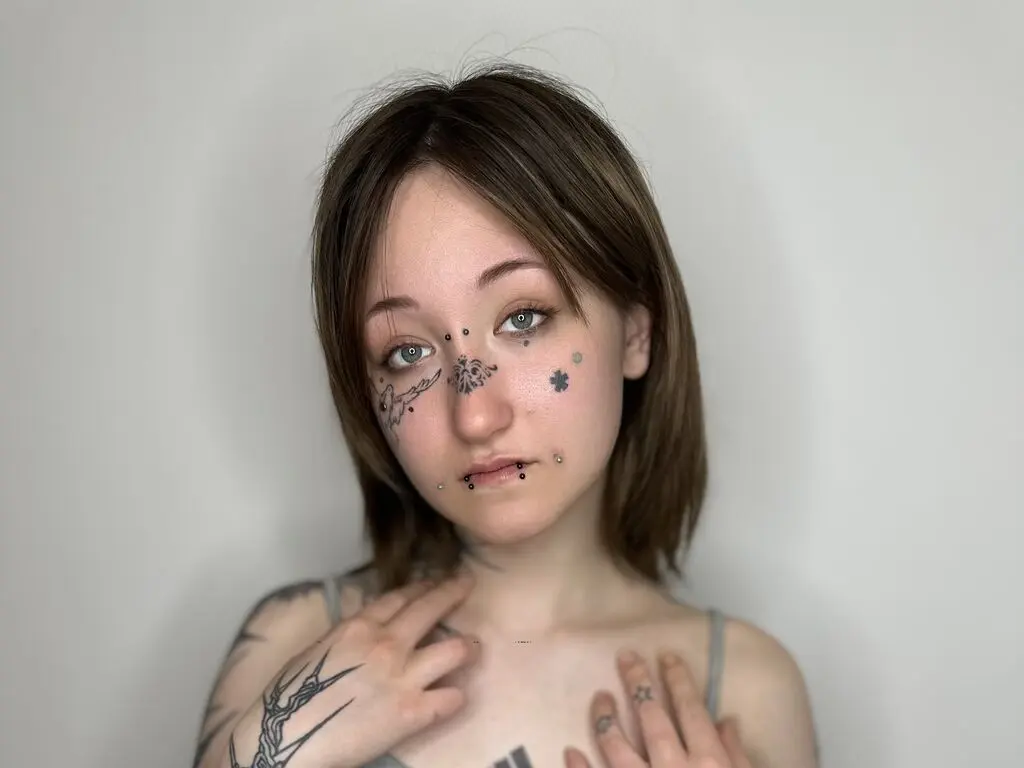 Young woman with facial tattoos and short brown hair posing against a plain white background.
