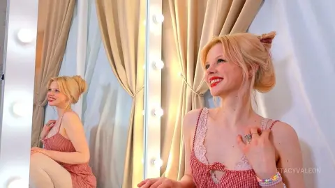 Smiling blonde woman in a red gingham sundress posing in a bright dressing room mirror.
