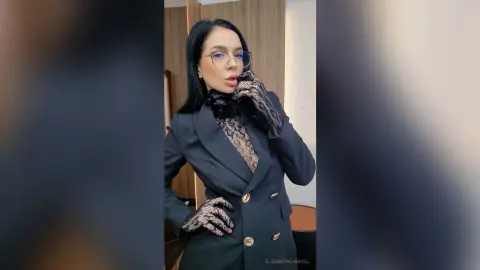 ElizabethChantal — Stylish woman in a black blazer and patterned mesh gloves posing confidently in a modern indoor setting.