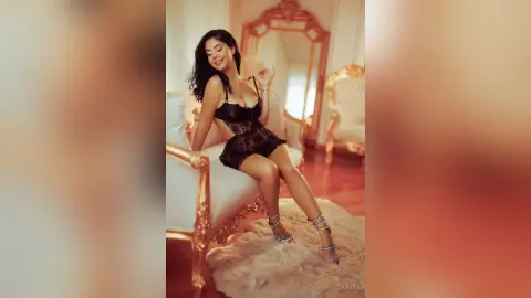 Smiling woman in black lace lingerie sitting on a white vintage sofa in a luxurious gold room.
