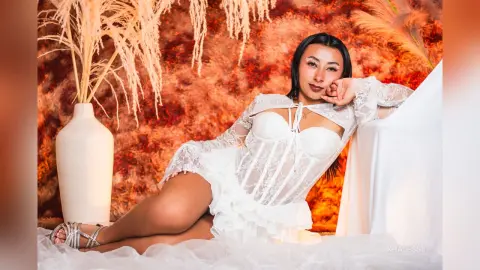 Woman in white lace corset outfit reclining against a white cloth in a warm, dreamy autumnal setting.
