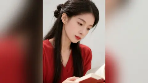 Serene young woman in a red v-neck top reading a book in a bright, minimalist indoor setting.