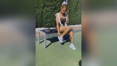 Young woman in a brown mini dress and white sneakers sitting on a bench outdoors in a relaxed summer mood.