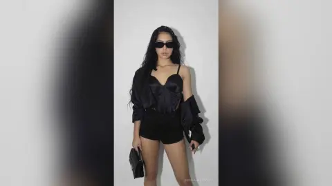 Stylish woman in a black satin corset and shorts posing in a minimalist studio setting with a chic moody vibe.