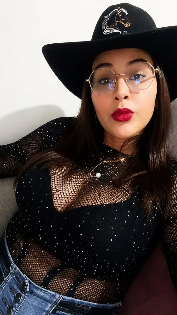 Parisannee poses with a pouty expression, showing her long dark hair and wearing round glasses in a close-up shot.