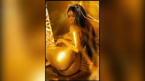 KeianHoz poses naked with gold paint covering her body against a dark background.