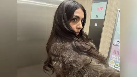 Glamorous woman with long dark hair wearing a luxury faux fur coat in a modern elevator.
