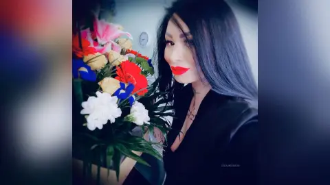 DeeaAnderson poses with a large, colorful bouquet of red, pink, and white flowers, wearing a black top with her long dark hair down.