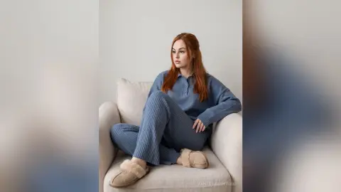 Redheaded woman in blue ribbed loungewear relaxing in a cozy white armchair.