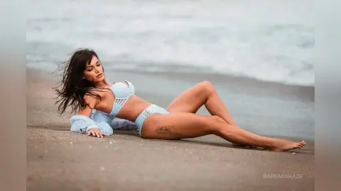 Young woman in light blue bikini relaxing on a sandy beach by the ocean waves under soft natural light.