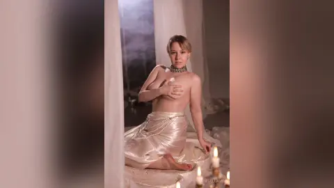 Blonde woman in a satin skirt and silver choker posing gracefully in a dreamy, candlelit room.