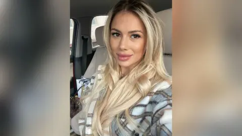 Blonde woman in a cozy plaid coat sitting in a car with a soft, glamorous aesthetic.