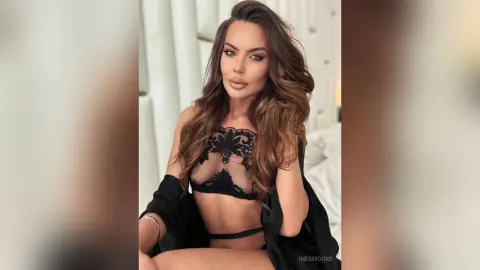 Glamorous woman in black lace lingerie and a robe posing in a bright, modern bedroom.