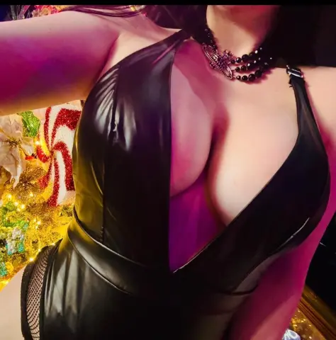 Woman in a black leather halter bodysuit posing in a festive holiday setting with warm lighting.