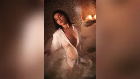 VickyPortman relaxes in a bubble bath wearing a sheer white open shirt that reveals her breasts and stomach.