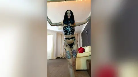 DeeaAnderson stands with her arms outstretched, wearing a black skeleton-style harness and black lace lingerie.