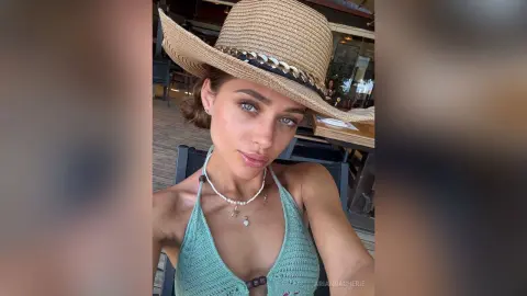 Young woman in a mint crochet halter top and straw hat relaxing at an outdoor cafe.