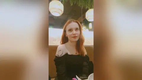 Redheaded woman in a black off-the-shoulder top sitting in a cozy cafe with warm hanging lights.
