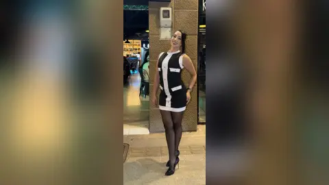 Smiling woman in a chic black and white sleeveless dress and tights standing in a modern urban setting.