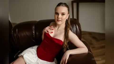 LiliLohan poses on a dark brown leather sofa wearing a red strapless corset and white skirt.