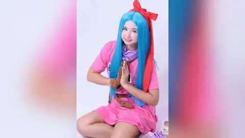 Smiling girl in blue wig and pink dress cosplay outfit posing against a white background.