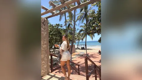 Smiling woman in white summer outfit enjoying a tropical beach vacation under palm trees.
