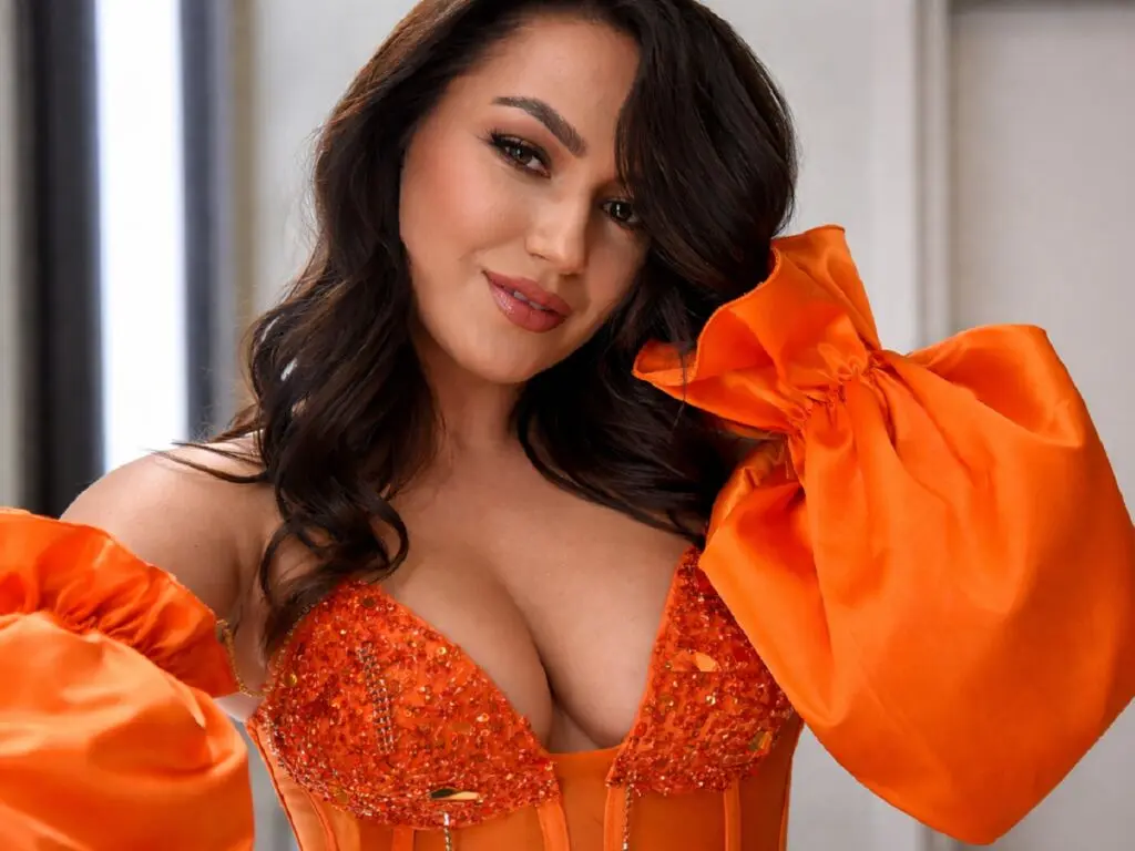 Beautiful woman in an elegant orange sequined puff-sleeve gown posing with a glamorous expression.