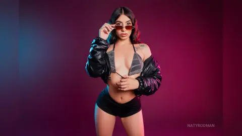 Confident woman in a black leather jacket and silver bikini top posing against a moody purple background.