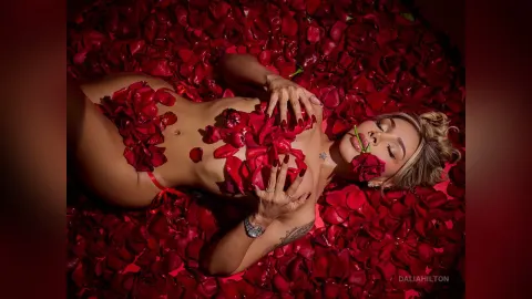 DaliaHilton — DaliaHilton lies naked on a bed of red rose petals, covering her breasts with the flowers.