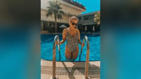 Blonde woman in a zebra print swimsuit relaxing by a sunny tropical resort swimming pool.