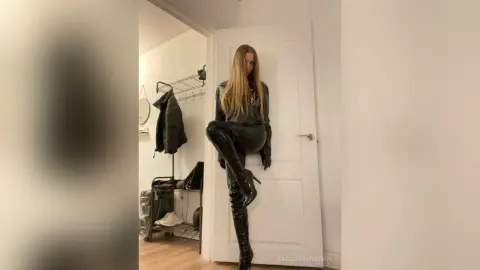 Fashionable woman in chic black leather outfit and tall boots posing in a minimalist modern room.