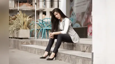 JessieLiu sits on stone steps wearing a white top, light grey vest, and black trousers with black high heels.