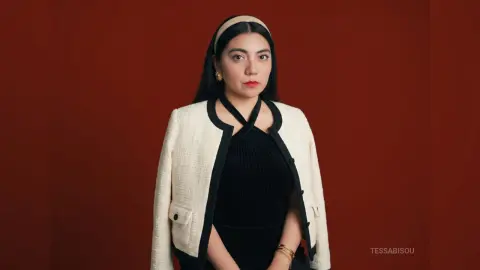 Elegant woman in a black velvet top and white tweed jacket posing against a deep red background.