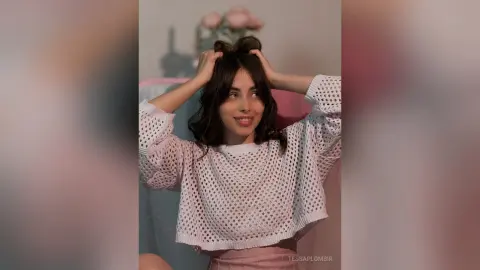 Smiling young woman in a white crochet knit sweater relaxing in a cozy, soft-lit indoor setting.