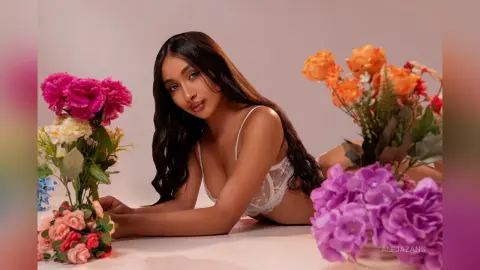 Beautiful woman in white lace lingerie lying amidst colorful flowers in a soft, romantic setting.