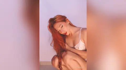 LaurentBelluci poses with her long red hair draped over her shoulder while wearing white lace lingerie.